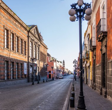 A street with a black pole with three lights on top. The street is empty and the buildings are old. City of Puebla, Mexico, crafts