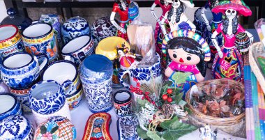 A table full of Mexican pottery and figurines. The table is covered with various items, including a large bowl, a vase, and a small figurine. City of Puebla, Mexico, crafts