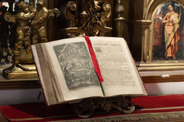 A book is open to a page with a red ribbon. The ribbon is tied to the book, and the book is on a stand. The book is old and has a gold frame. City of Puebla, Mexico, crafts