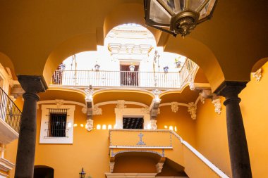 A large, ornate building with a yellow color scheme. The building has a large archway and a balcony, and the inside is filled with columns and arches. City of Puebla, Mexico, crafts