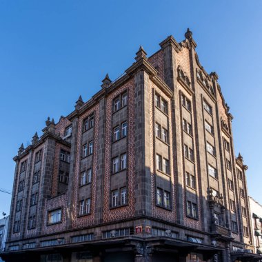 A large brick building with a red and white facade. The building has a lot of windows and a very tall roof. The building is located in a city. City of Puebla, Mexico, crafts