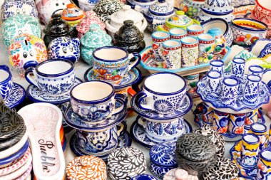 A table is filled with a variety of colorful ceramic items, including cups, saucers, and bowls. Some of the items have the word 