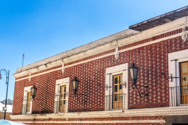 A brick building with a red roof and white trim. The building has a lot of windows and a balcony. City of Puebla, Mexico, crafts