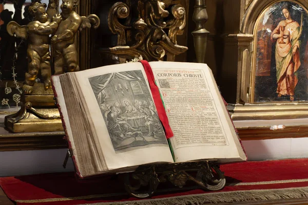 A book is open to a page with a red ribbon. The ribbon is tied to the book, and the book is on a stand. The book is old and has a gold frame. City of Puebla, Mexico, crafts
