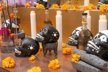 A table with skulls and candles on it. The skulls are black and white and the candles are lit. Day of the Dead celebration in Mexico, papel picado crafts, offerings, La Catrina