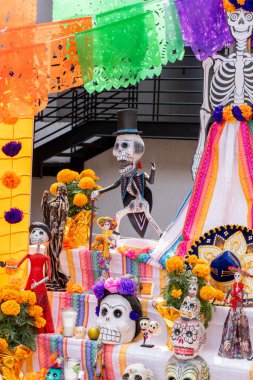 A festive arrangement of skeletons and skulls, including a man in a top hat, is on display for Dia de los Muertos. Day of the Dead celebration in Mexico, papel picado crafts, offerings, La Catrina
