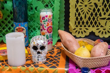 Kafatası, mumlar ve meyveli bir masa. Kafatası mumlar ve meyvelerle çevrilidir. Meksika 'da Ölüler Günü kutlaması, papel picado el sanatları, adaklar, La Catrina