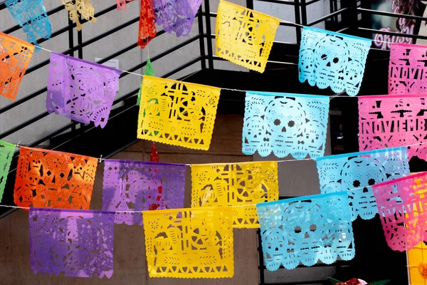 Üzerinde kafatasları olan renkli kağıt bayraklar. Bayraklar korkuluklardan sarkıyor. Meksika 'da Ölüler Günü kutlaması, papel picado el sanatları, adaklar, La Catrina