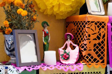 A shelf with a skeleton and a woman statue, a candle, and a vase with flowers.Day of the Dead celebration in Mexico, papel picado crafts, offerings, La Catrina