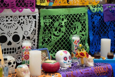 A table with a variety of colorful decorations, including candles, skulls, and flowers. Day of the Dead celebration in Mexico, papel picado crafts, offerings, La Catrina