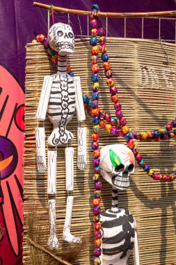 A skeleton is hanging from a bamboo pole with a colorful string. The skeleton is decorated with paint. Day of the Dead celebration in Mexico, papel picado crafts, offerings, La Catrina