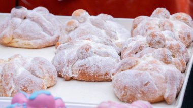 A tray of doughnuts with powdered sugar on top. The doughnuts are arranged in a row and are all different sizes. Day of the Dead celebration in Mexico, papel picado crafts, offerings, La Catrina