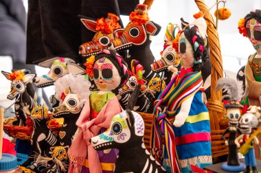 A collection of dolls with Mexican designs and skulls. The dolls are arranged in a basket. Day of the Dead celebration in Mexico, papel picado crafts, offerings, La Catrina