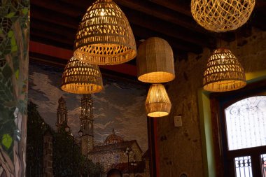 A room with a mural on the wall and several hanging lamps. The lamps are made of bamboo and have a warm, cozy feel to them. Mexico, zacatlan de las manzanas, puebla, day of the dead mexican tradition