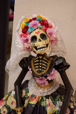 A skeleton dressed in a white veil and a floral dress. The skeleton is smiling and has a flower on its head. Mexico, zacatlan de las manzanas, puebla, day of the dead mexican tradition