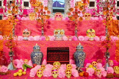 A table with a pink background and a pink tablecloth. There are many skulls and flowers on the table. Mexico, zacatlan de las manzanas, puebla, day of the dead mexican tradition