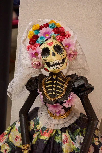A skeleton dressed in a white veil and a floral dress. The skeleton is smiling and has a flower on its head. Mexico, zacatlan de las manzanas, puebla, day of the dead mexican tradition