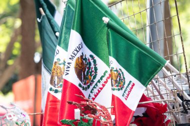 A row of Mexican flags are hanging on a fence. The flags are green, white, and red. Decoration to celebrate Independence Day in Mexico, zocalo