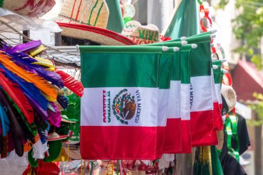 A row of flags with the word Mexico on them. The flags are hanging on a rack. The flags are colorful and have a festive feel to them. Decoration to celebrate Independence Day in Mexico, zocalo