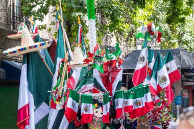 A group of flags and hats are displayed on a street. The flags are of different colors and sizes, and the hats are of various styles. Decoration to celebrate Independence Day in Mexico, zocalo