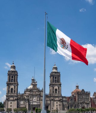 A large flag with the colors red, white, and green is flying in front of a large building. Decoration to celebrate Independence Day in Mexico, zocalo