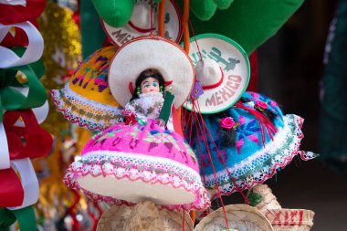 A collection of Mexican dolls are hanging from a string. The dolls are dressed in colorful clothing and are wearing sombreros. Decoration to celebrate Independence Day in Mexico, zocalo