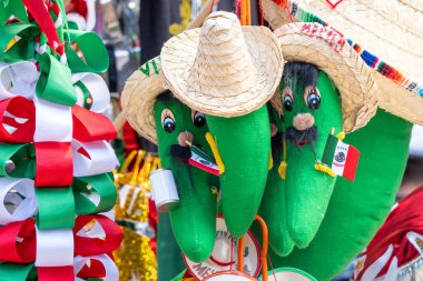 Two green peppers with hats on them and flags on their hats. The peppers are hanging from a string. Decoration to celebrate Independence Day in Mexico, zocalo