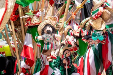 A collection of Mexican dolls and hats are displayed. The dolls are dressed in traditional Mexican clothing and are hanging from a pole. Decoration to celebrate Independence Day in Mexico, zocalo