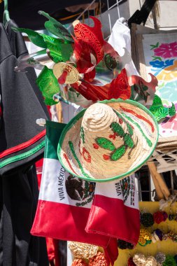 A Mexican flag is hanging next to a hat. The hat is decorated with green, red, and white colors. Decoration to celebrate Independence Day in Mexico, zocalo