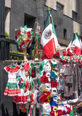 A colorful display of Mexican clothing and accessories. The display is set up outside of a building. The flags are in the background. Decoration to celebrate Independence Day in Mexico, zocalo