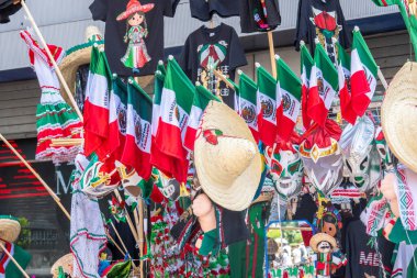 A store with flags and hats for sale. The flags are red, white, and green. The hats are straw and have a flower on them. Decoration to celebrate Independence Day in Mexico, zocalo