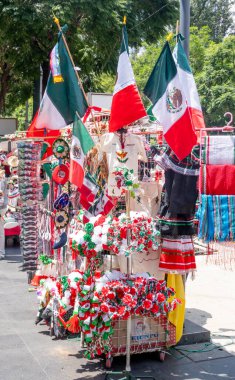 A display of Mexican flags and other items. The flags are in various sizes and colors. The display is set up on a sidewalk. Decoration to celebrate Independence Day in Mexico, zocalo
