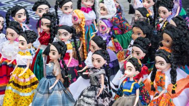 A group of dolls are lined up, some wearing traditional Mexican clothing. The dolls are of various sizes and colors. Decoration to celebrate Independence Day in Mexico, zocalo