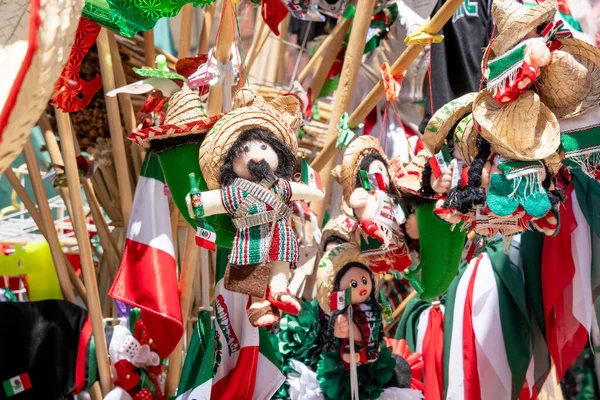 A collection of Mexican dolls and hats are displayed. The dolls are dressed in traditional Mexican clothing and are hanging from a pole. Decoration to celebrate Independence Day in Mexico, zocalo