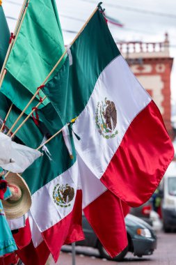 Flags of Mexico are hanging on a pole. The flags are red, white, and green. Historic center of Queretaro City, decorations and traditions to celebrate Mexico's Independence Day, colonial architecture, alleys and facades