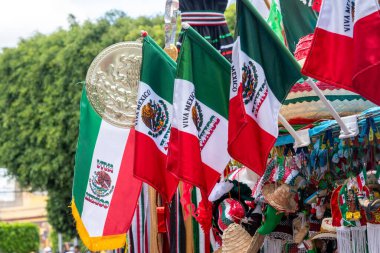 A collection of Mexican flags and hats are displayed. The flags are red, white, and green. Historic center of Queretaro City, decorations and traditions to celebrate Mexico's Independence Day, colonial architecture, alleys and facades