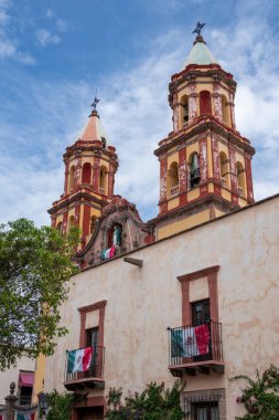 The two tall buildings are painted in red and yellow colors. They are situated in a foreign country. Historic center of Queretaro City, decorations and traditions to celebrate Mexico's Independence Day, colonial architecture, alleys and facades