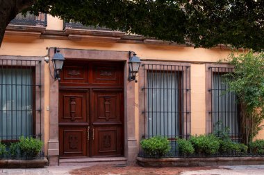 Sarı bir binanın önünde pirinç saplı büyük bir ahşap kapı vardır. Queretaro şehrinin tarihi merkezi, Meksika 'nın Bağımsızlık Günü' nü, sömürge mimarisini, sokaklarını ve cephelerini kutlamak için dekorasyon ve gelenekler