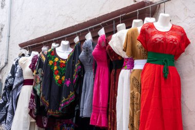 A rack of clothing with a variety of colors and styles. The clothes are hanging on a wall. Historic center of Queretaro City, decorations and traditions to celebrate Mexico's Independence Day, colonial architecture, alleys and facades