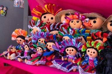 A group of dolls with various outfits and accessories are displayed on a pink surface. Historic center of Queretaro City, decorations and traditions to celebrate Mexico's Independence Day, colonial architecture, alleys and facades