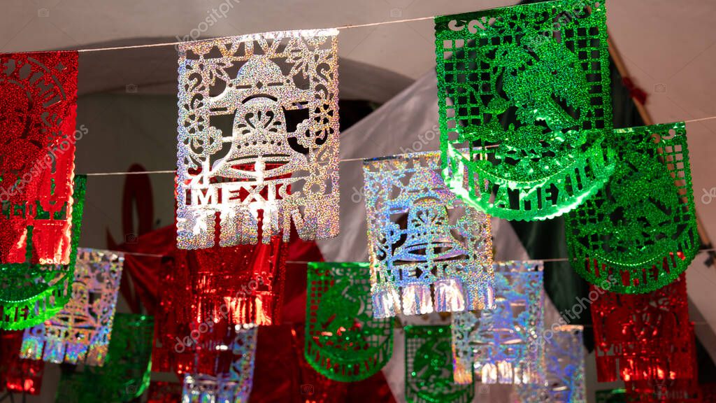 A collection of paper lanterns in the shape of Mexican flags are hanging from a string, creating a f. Historic center of Queretaro City, decorations and traditions to celebrate Mexico's Independence Day, colonial architecture, alleys and facades