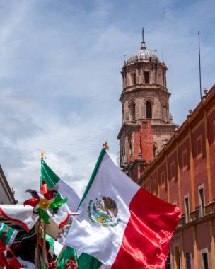 Flags of Mexico are flying in the air in front of a tall building. The flags are red, white. Historic center of Queretaro City, decorations and traditions to celebrate Mexico's Independence Day, colonial architecture, alleys and facades