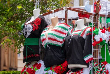 A rack of clothing with a woman's body on it. The clothes are colorful. Historic center of Queretaro City, decorations and traditions to celebrate Mexico's Independence Day, colonial architecture, alleys and facades