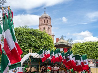 A large group of flags are displayed in front of a church. The flags are of different colors. Historic center of Queretaro City, decorations and traditions to celebrate Mexico's Independence Day, colonial architecture, alleys and facades