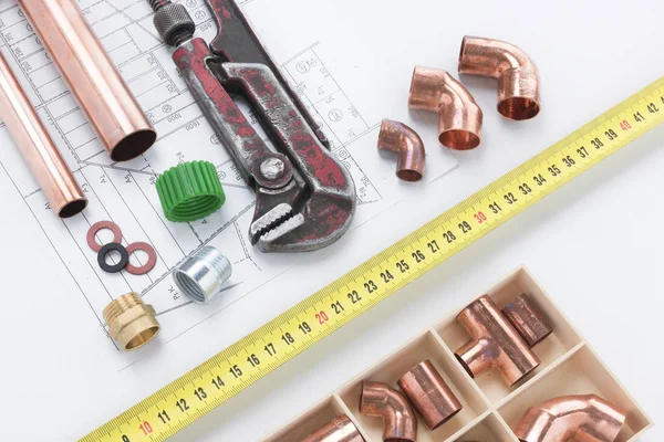 Copper pipes and elbow joints, pipe wrench, and tape measure on a white background