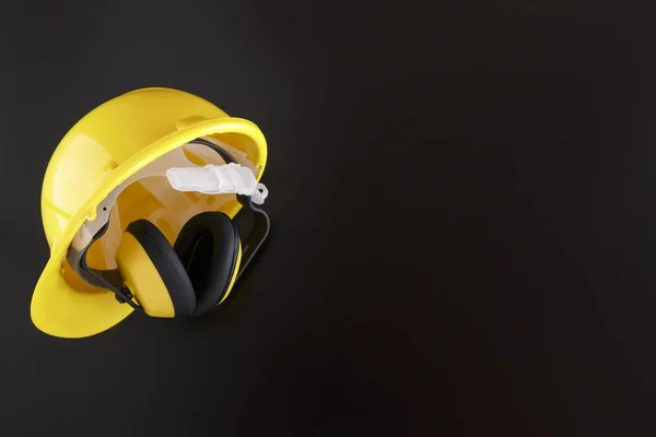Earmuffs and yellow hard hat on a black background with copy space