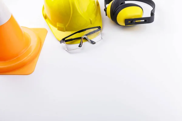 Construction protective gear including hard hat, safety goggles, and earmuffs with a traffic cone on a white background with copy space