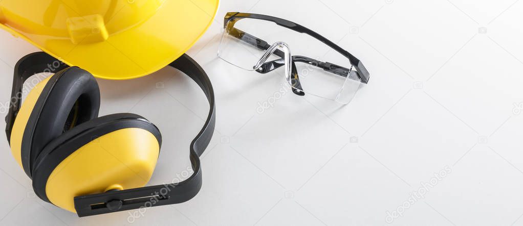 Construction safety equipment including hard hat, earmuffs, and protective goggles on white background banner image with copy space