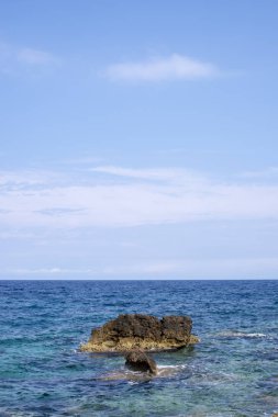 Berrak mavi gökyüzü altında sakin mavi denizin ortasında küçük kaya oluşumu