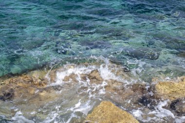 Kıyıdaki kayalara çarpan deniz suyunun tepeden görünümü